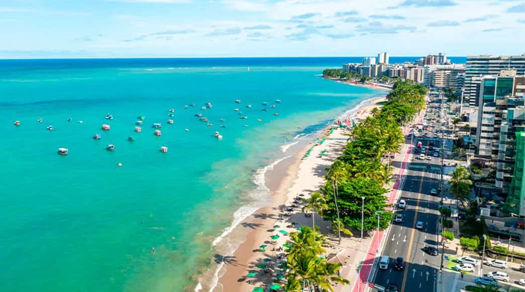 Praia de Ponta Verde em Maceió com mar azul-turquesa, coqueiros, areia clara e orla urbana ao fundo.